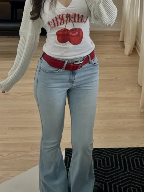Try-on with a cream cardigan, cherry-print top, red belt, and light blue flared jeans